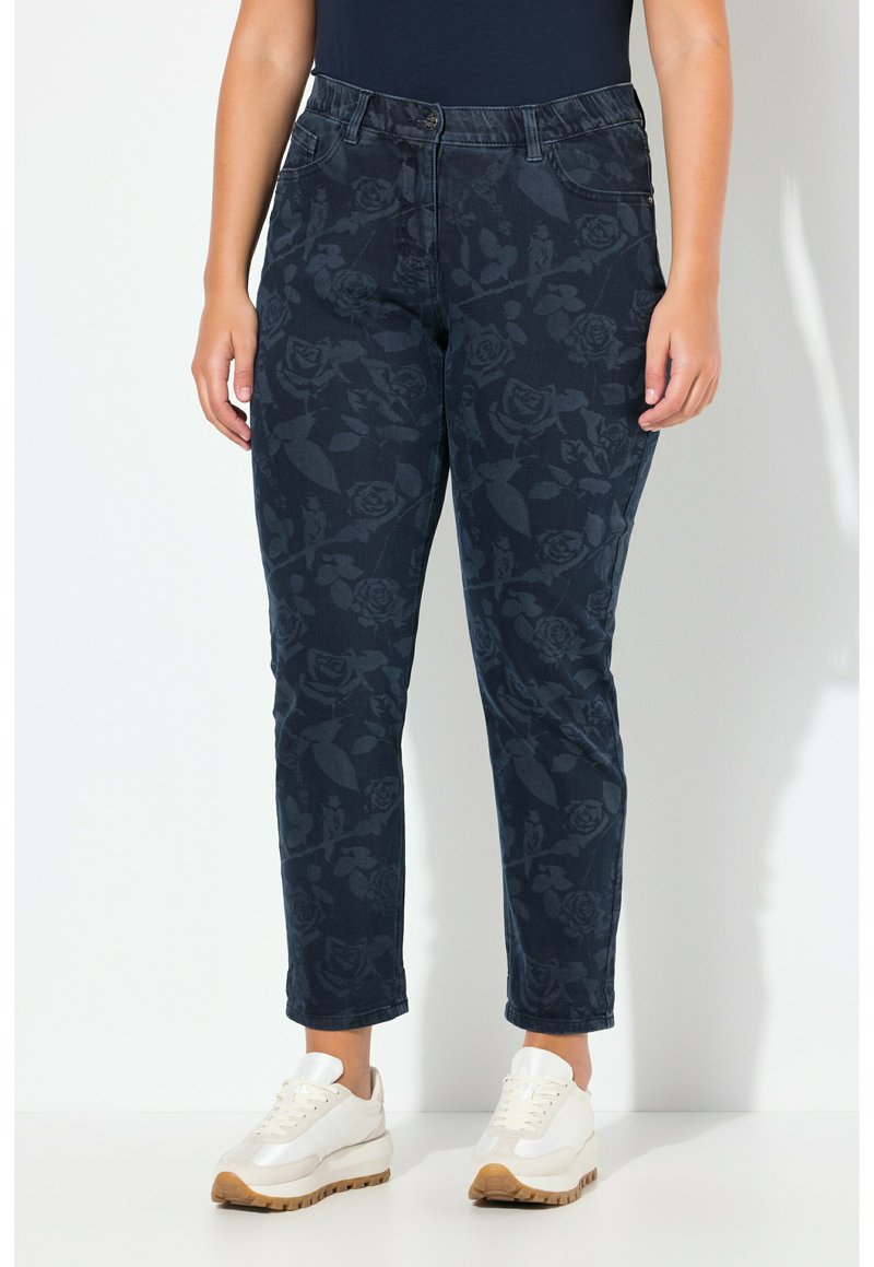 Tmavě modré džíny s květinovým vzorem, hladkým povrchem, vysokým pasem, rovně střižené a s pěti kapsami. Nosené s bílými teniskami.