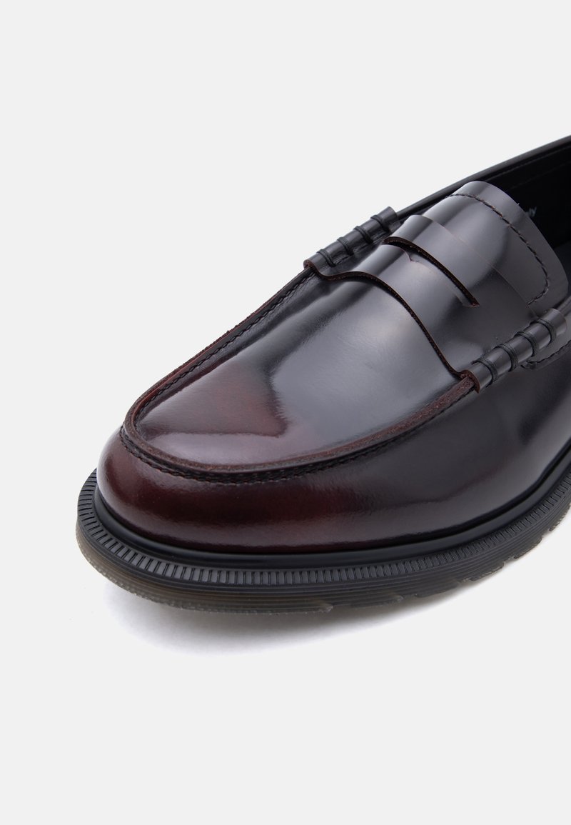 Dunkelbrauner, polierter Leder-Pennyloafer mit schwarzer Gummisohle und detaillierter Naht auf weißem Hintergrund.