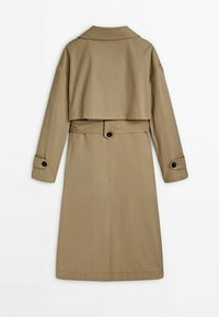 Trench-coat long beige avec patte de dos, ceinture avec détail bouton et sangles de manches boutonnées, vu de dos sur fond blanc.