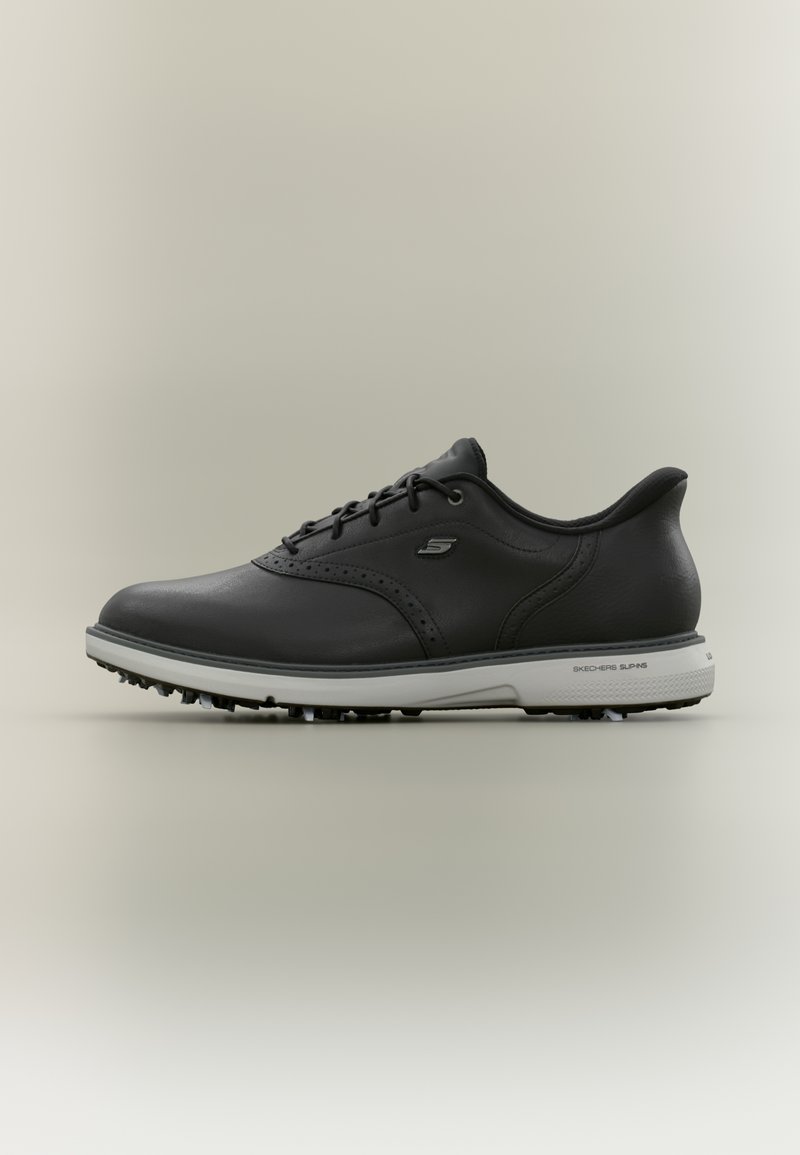 Chaussure de golf noire en cuir à lacets avec semelle blanche équipée de petits crampons et logo Skechers sur le côté et la semelle.
