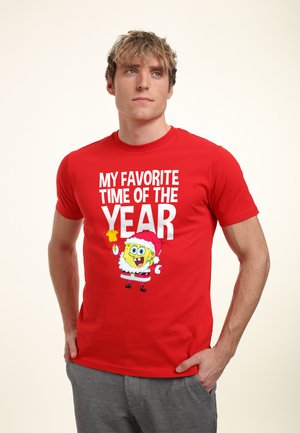 Rød bomulds T-shirt med et grafisk motiv af en juletema tegneseriefigur med teksten "MIT FAVORIT TID PÅ ÅRET" i hvid.