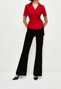 Haut rouge à manches courtes et effet portefeuille avec un décolleté en V, associé à un pantalon noir évasé. Chaussures noires à talons élégantes.