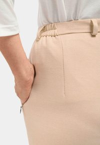 Pantalons tissés beiges avec une taille élastique et une poche latérale, mettant en valeur un tissu texturé et une silhouette épurée.