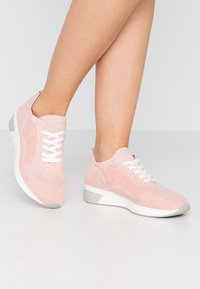 Světle růžové pletené tenisky s bílými tkaničkami, texturovaným svrškem a šedým akcentem na patě. Nízký střih a flexibilní podrážka.