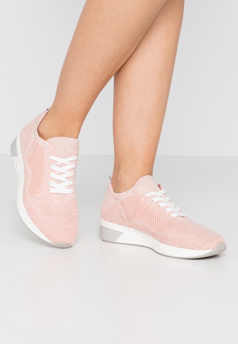 Světle růžové pletené tenisky s bílými tkaničkami, texturovaným svrškem a šedým akcentem na patě. Nízký střih a flexibilní podrážka.