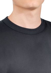 Svart t-shirt med rund halskrage tillverkad av mjuk bomullstyg. Har en ribbad krage och en enkel design. Närbild av halsringning och övre bröst.