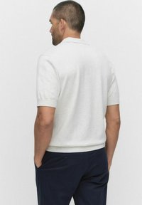Lichtgrijze polo met korte mouwen en een geribbelde kraag en manchetten, met een gladde textuur en een aansluitende pasvorm. Draagt bij een marineblauwe broek.