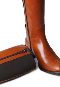 Botte haute en cuir marron avec une finition brillante et une fermeture éclair sur le côté, accompagnée d'une pochette zippée marron et noire. Texture lisse et design simple.