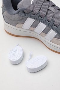 Sneaker in suede grigio con strisce e lacci bianchi, caratterizzato da una parte superiore texturizzata e suola in gomma. Inclusi due lacci bianchi aggiuntivi.