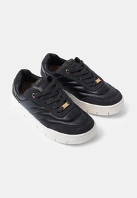 Black leather sneakers with textured panels, lace-up design, gold hardware accents, and thick white rubber sole.