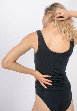 Canottiera nera con scollatura a goccia e design aderente, realizzata in tessuto morbido. Indossata con un perizoma nero abbinato, che mette in risalto una silhouette slanciata.