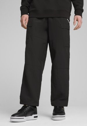 Black cargo pants made of lightweight fabric, featuring two side pockets, loose fit, and minimal stitching details. Paired with black sneakers.