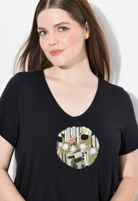 Zwarte T-shirt met korte mouwen, voorzien van een cirkelvormig, multikleurig geborduurd design met verschillende patronen en texturen, en een V-hals.