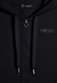 Hoodie zippé bleu marine avec fermeture éclair métallique et cordons de serrage. Présente le logo "FREDDY" en strass sur la poitrine. Tissu doux et extensible.