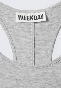 Gros plan sur un col en tissu gris avec une étiquette de marque "WEEKDAY" cousue, centrée sur la couture du col à l'arrière.