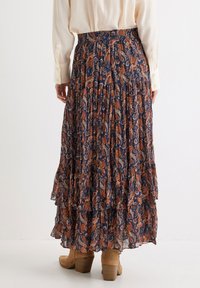 Falda maxi fluida y en capas en color navy con estampado de paisley en naranja y crema. Tejido ligero, cintura elástica y dobladillo con volantes.