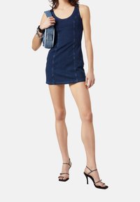 Jeansminiklänning med en fitted form, mörkblå färg och ärmlös design. Matchad med strappy svarta klackar som har nitar.