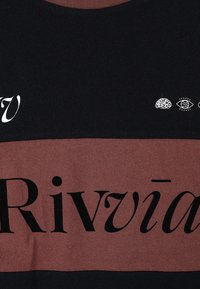 Pamucna majica sadrži horizontalne crne i bordo pruge, veliki crni natpis "Rivìa" te male bijele grafike mozga i oka.