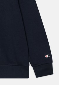 Granatowy sweter z ryżowym mankietem i pasem. Posiada małe, białe i czerwone logo na lewym rękawie. Wykonany z miękkiego materiału bawełnianego.
