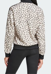 Leopardmönstrad bomberjacka med beige bas, svarta ribbade muddar och nederdel, samt kontrasterande svart krage. Mjukt tyg.