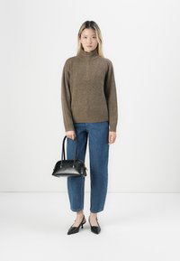 Maglione marrone a maglia con colletto alto, jeans in denim blu, borsa nera e tacchi neri. La trama è a coste e l'outfit include forme classiche.