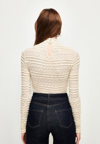 Langærmet creme top med teksturerede striber og en nøglehul detalje i ryggen, parret med højttaljede mørke denim jeans med baglommer.