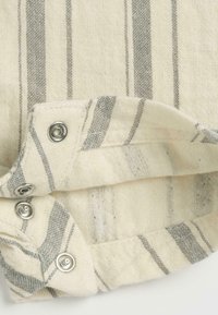 Tissu rayé en tons crème et gris avec des boutons-pression en métal. La texture est tissée, offrant une finition douce et naturelle.