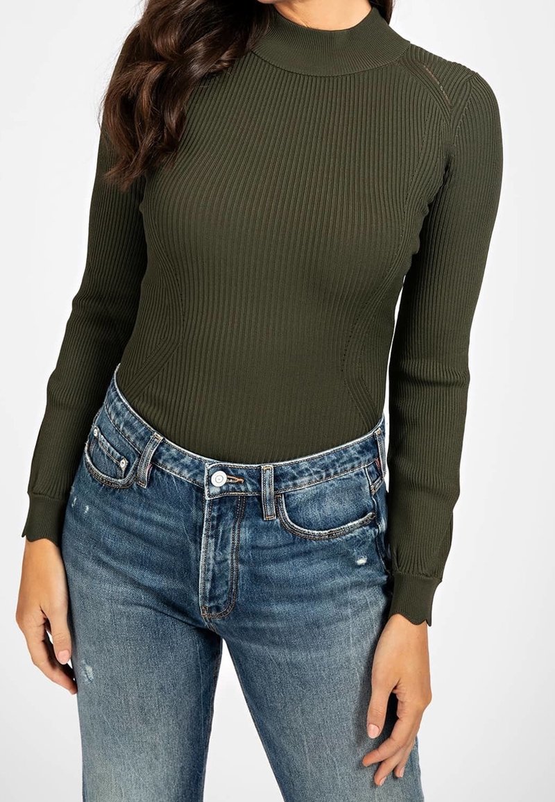 Olivengroene geribbelde longsleeve top met een hoge hals, gecombineerd met een blauwe versleten denim jeans met een klassieke pasvorm en knoopsluiting.