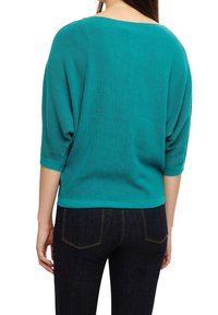 Turkusowy, prążkowany sweter z szerokim, okrągłym dekoltem i rękawami o długości 3/4. Luźny krój, teksturowany materiał, noszony z ciemnymi dżinsami.