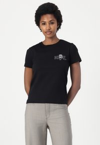 Svart bomull T-skjorte med et lite hvitt grafisk trykk med "KARL" og en astronautdesign på venstre bryst. Korte ermer, rund hals.