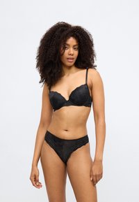 Melna mežģīņu krūšturis ar stīpiņām un regulējamām lencītēm, kopā ar saskaņotām mežģīņu biksītēm ar viļņotu malu. Vienkāršs ziedu raksts.