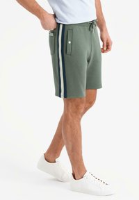 Shorts in cotone verde con vita a cordoncino, dotati di due tasche laterali, strisce blu navy e crema sui lati e vestibilità comoda.