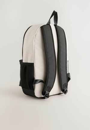 Rygsæk med en beige stofkrop, sorte polstrede skulderstropper og en sidelomme af netmateriale. Har sorte detaljer og et bærehåndtag i toppen.