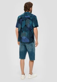 Korte mouwen shirt met een blauw en groen abstract patroon, gecombineerd met spijkerbroek shorts. Witte sneakers maken de casual outfit compleet.