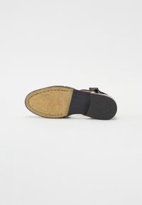 Shoe sole featuring a tan, textured cork insole, black outer sole, and leather strap with silver hardware.