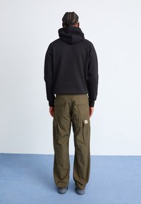 Sweatshirt à capuche noir avec une poche kangourou, associé à un pantalon cargo vert olive doté de poches latérales et d'un patch logo.