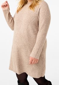 Strickkleid in Beige mit geripptem Muster und diagonalem Design. Langer Ärmeln und rundem Halsauschnitt, endet oberhalb des Knies.