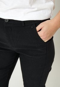 Person wearing black pants with hand in pocket and a white shirt tucked in at the waist.