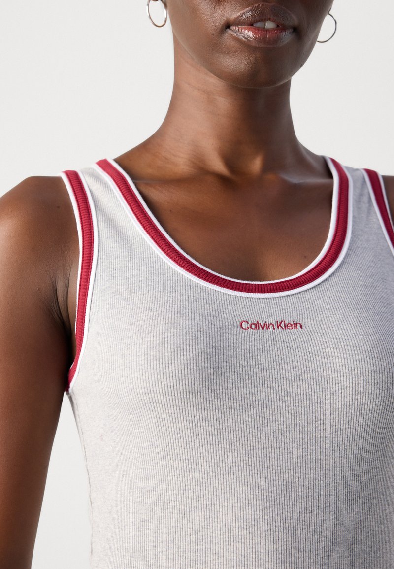 Graues geripptes Tanktop mit rotem und weißem Saum. Verfügt über ein kleines rotes "Calvin Klein"-Logo nahe dem Ausschnitt. Weiche Textur und figurbetontes Design.