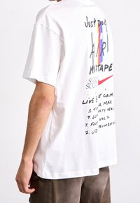 Vit bomullströja med grafisk design som har en regnbåge och text, inklusive "Just Do It" och "Mixtape." Korta ärmar, avslappnad passform.