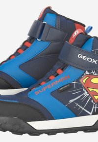 Sneakers alti blu e neri con dettagli rossi, caratterizzati da un logo di Superman e un design a fantasia. Chiusura con cinturino in Velcro regolabile.