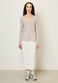 Svetlo béžový top s dlhým rukávom, skombinovaný s bielou džínsovou sukňou a sivými športovými topánkami, s akcentovým šitím a kontrastnými ponožkami.