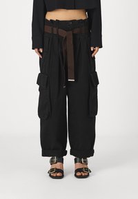 Černé cargo kalhoty s širokými nohavicemi, s hnědým pásem, velkými bočními kapsami a ohrnutými manžetami. Doplňuje je černé sandály a zlaté kovové doplňky.