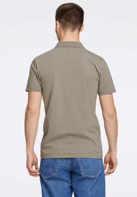 Oliven grøn polo skjorte med kort krave, korte ærmer og et let tekstureret stof, parret med blå denim jeans.