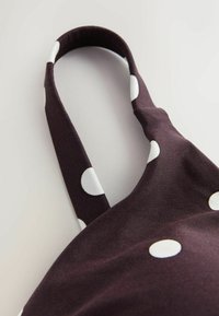 Dunkelbrauner Stoff mit großen weißen Punkten; verfügt über einen abgerundeten Tragegurt. Glatte Textur, vielseitiges Design für verschiedene Verwendungszwecke geeignet.