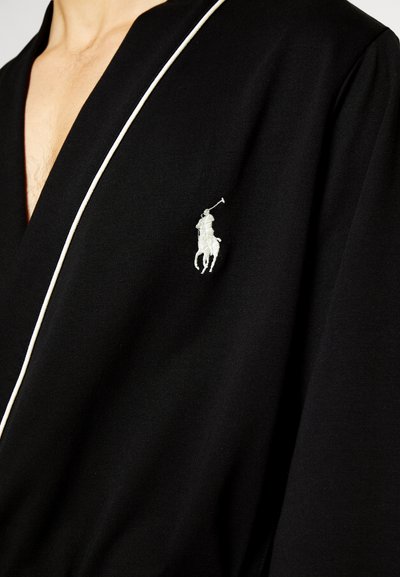 Zwarte robe met witte bies, gemaakt van zachte stof. Heeft een klein geborduurd logo van een ruiter op het linkerborstgedeelte.