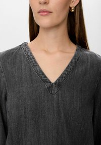 Top in denim grigio scuro con scollatura a V, caratterizzato da una finitura testurizzata e dettagli di cucitura in vista.