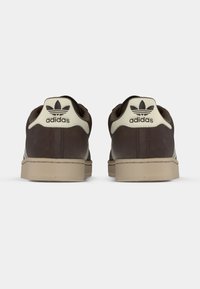Zapatillas deportivas de cuero marrón con detalles beige, puntera redondeada, suela plana y lengüeta de talón con el logo de Adidas.