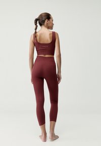 Bordový rebrovaný športový set obsahujúci skrátené tielko s výrezom a legíny s vysokým pásom, obidve v priliehavom strihu.