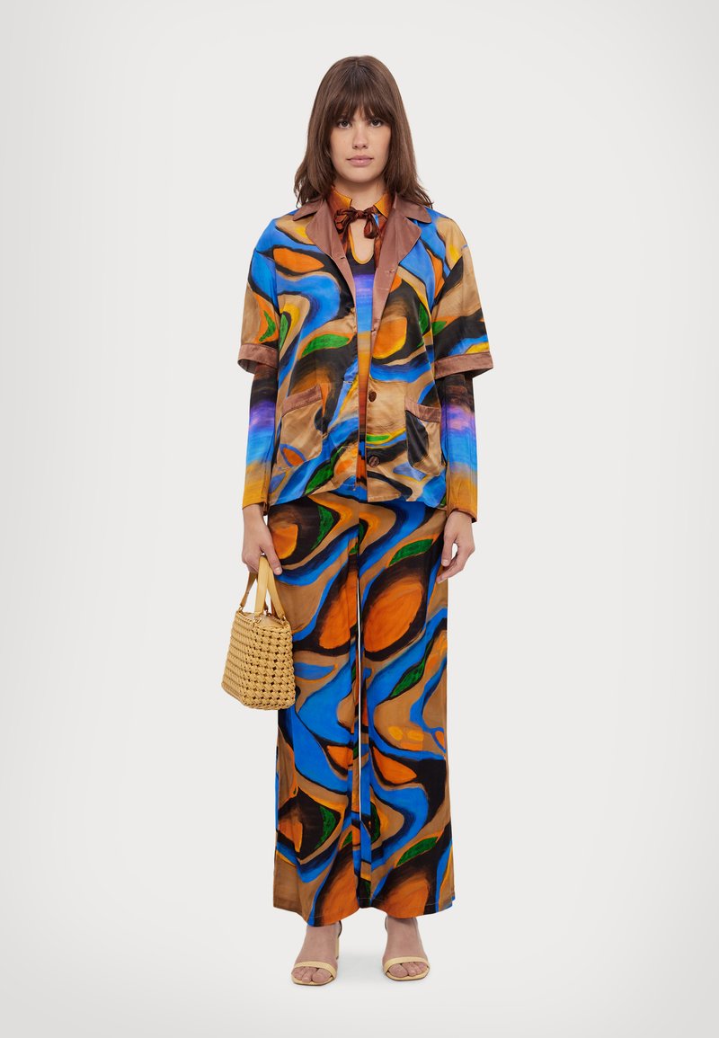 Kolorowy, wzorzysty dwuczęściowy strój w żywych odcieniach niebieskiego, pomarańczowego i brązowego; składa się z koszuli z krótkim rękawem na guziki oraz szerokich spodni, zestawiony z plecioną torbą.